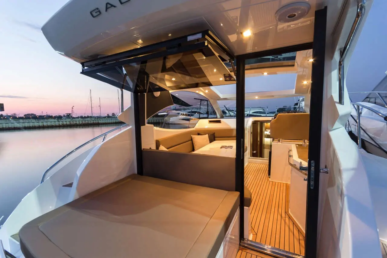 Luxury yacht interior showcasing a spacious lounge area, large windows, and evening lighting against a serene harbor backdrop.