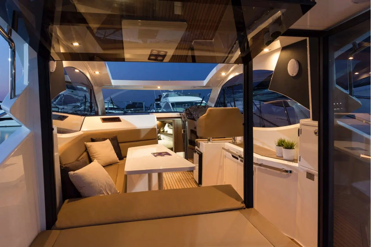Modern yacht interior featuring a cozy seating area, dining table, and helm, illuminated in evening light.