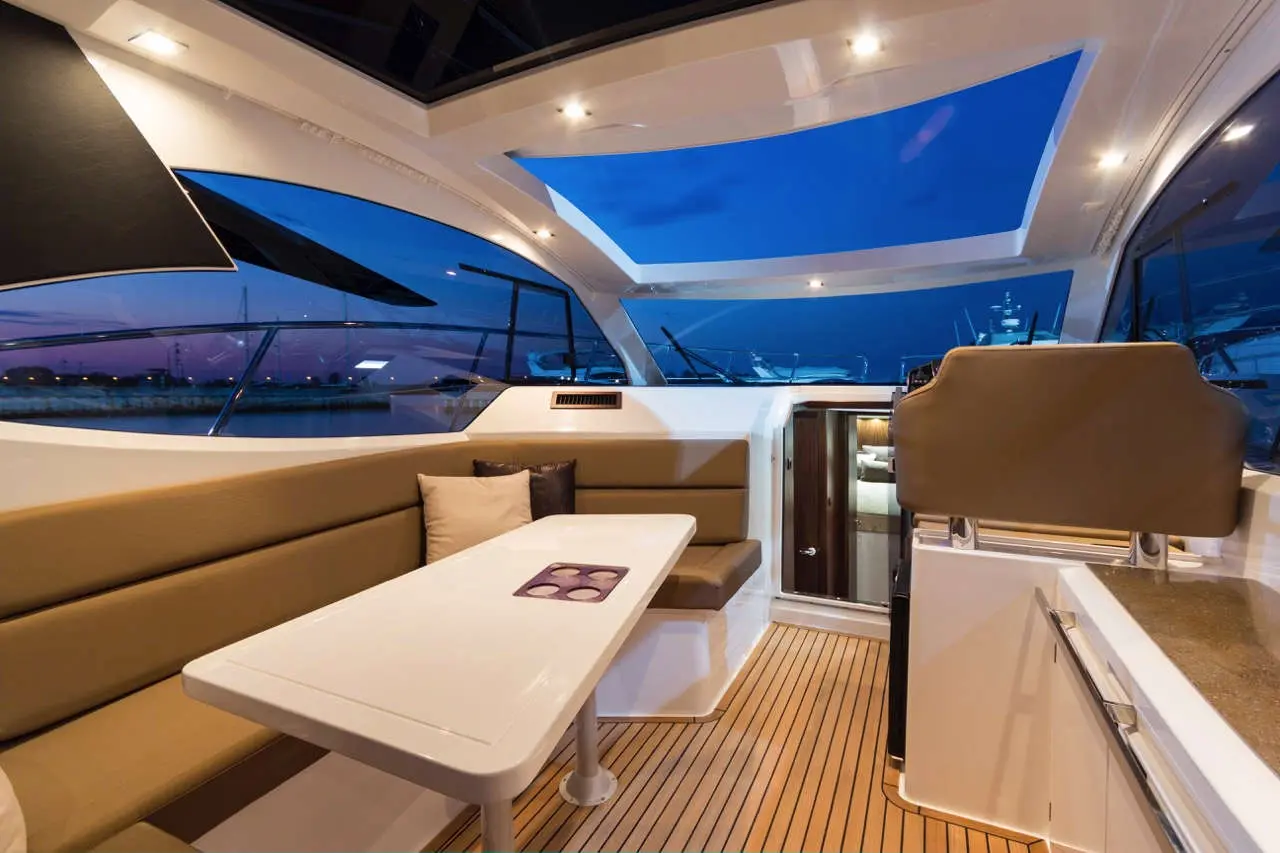 Modern boat interior featuring a dining area, large windows, and a night sky view, with a small table and sofa seating.