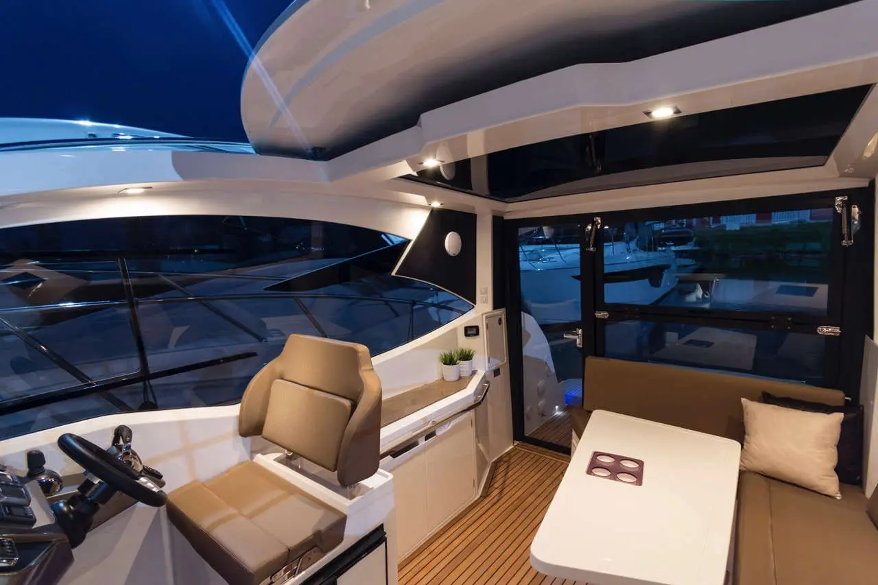 Luxury yacht interior featuring a modern helm, chic seating area, and panoramic windows overlooking the marina at night.