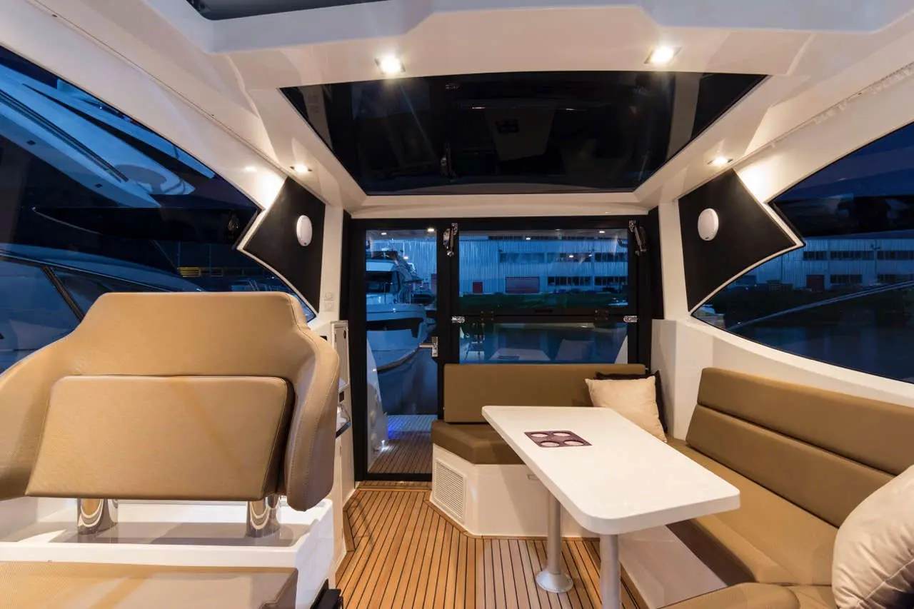 Modern boat interior featuring seating, a dining table, and large windows overlooking the marina at dusk.