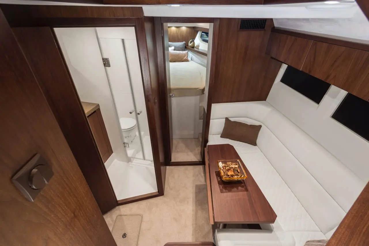 Luxury boat interior featuring a sitting area, kitchenette, bathroom with shower, and a cozy bedroom beyond.