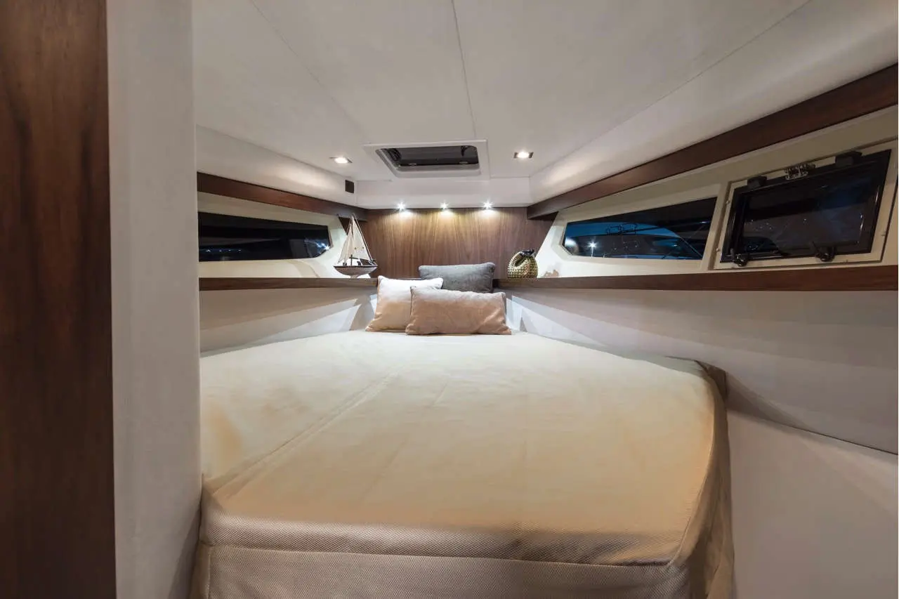 Cozy boat cabin with a queen-sized bed, decorative pillows, shelves, and a small sailboat model on the wall.