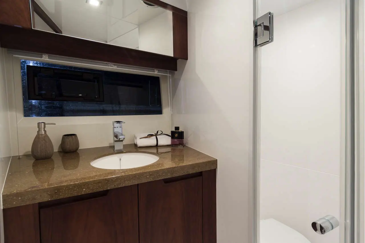 Modern bathroom featuring a brown wooden cabinet, round sink, mirror, and toiletries on a granite countertop.