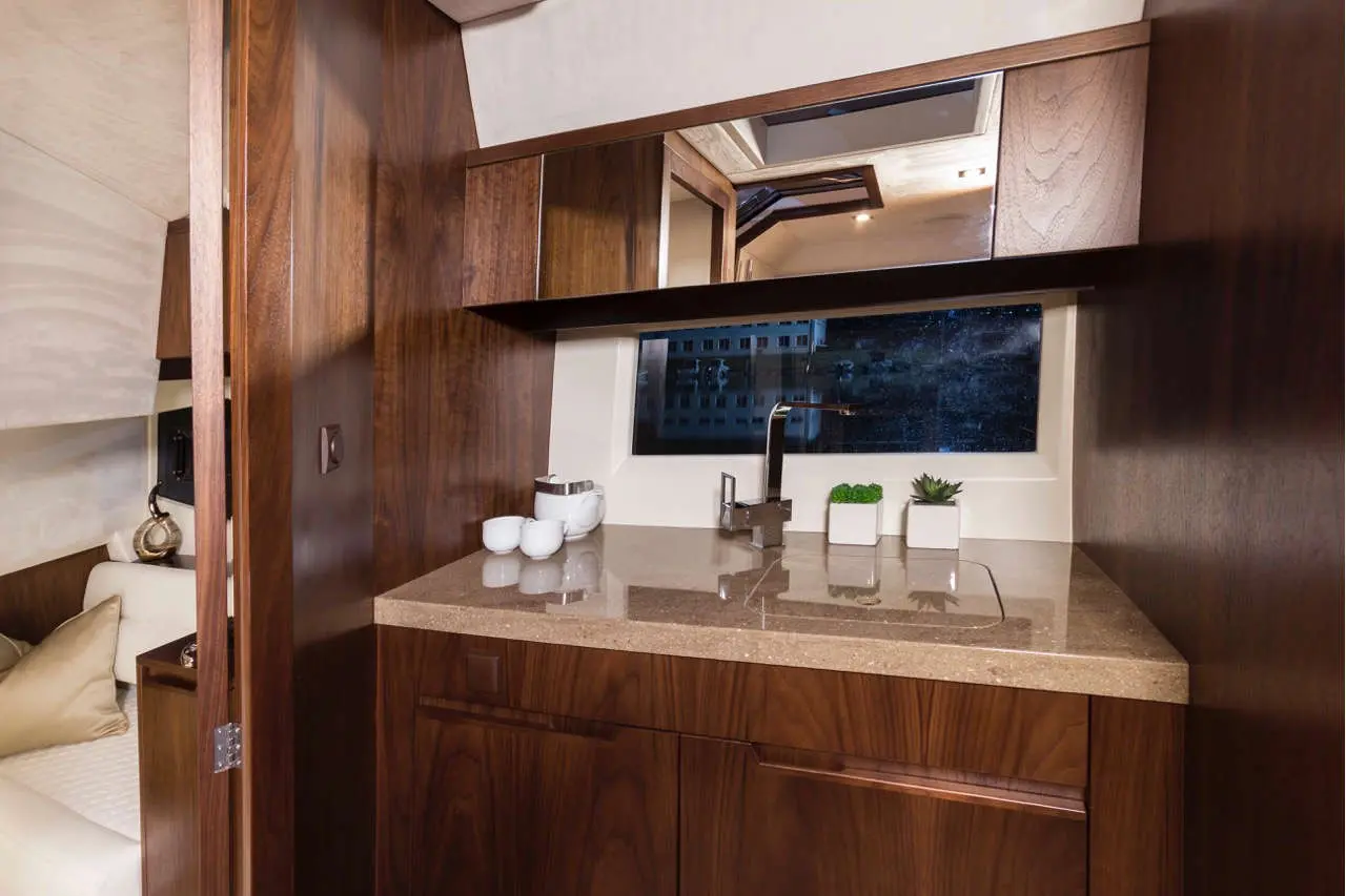 Modern kitchen area in a yacht featuring wooden cabinetry, a sink, and decorative plants by a large window.