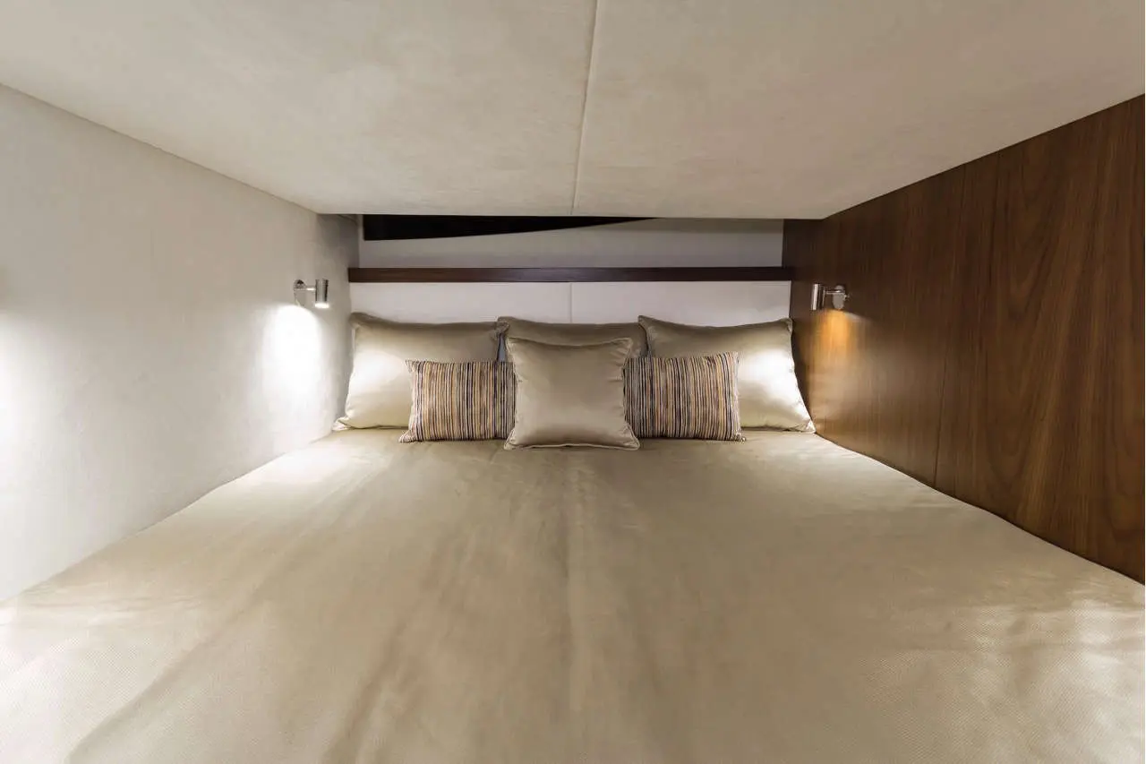 A cozy bed with soft beige bedding, decorative pillows, and warm bedside lights in a modern interior space.