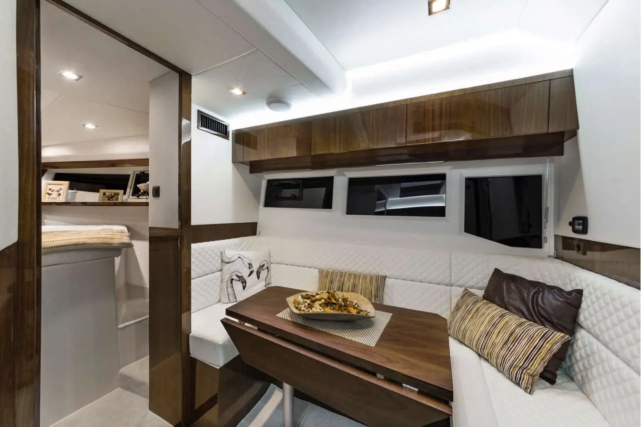 Modern yacht interior featuring a dining area with a wooden table, cushions, and decorative food presentation.