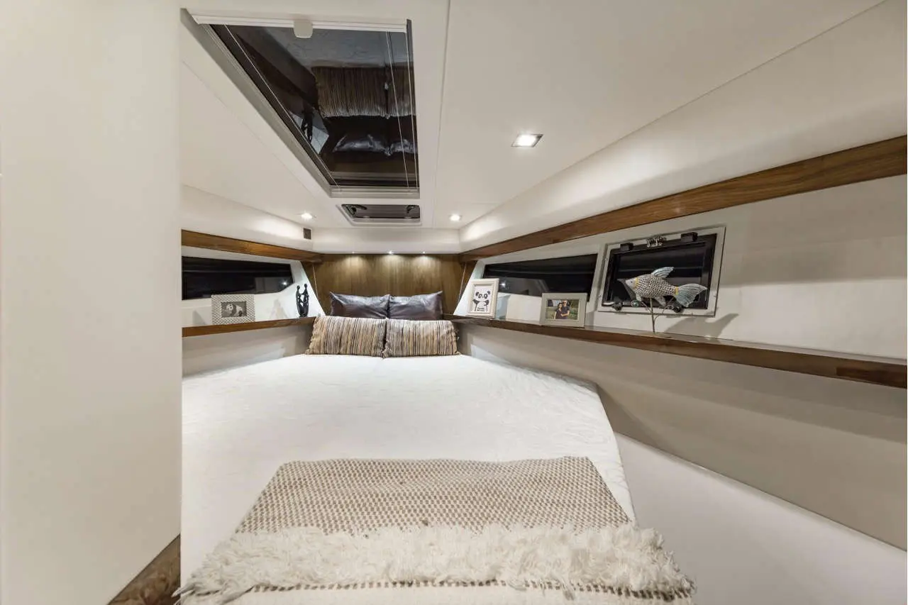 Modern boat cabin featuring a large bed, decorative pillows, art pieces, and natural light from overhead windows.