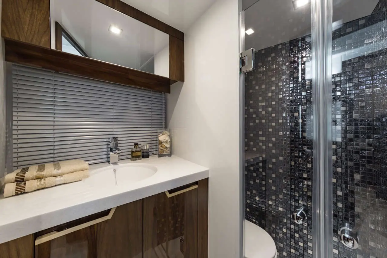 Modern bathroom featuring a sink, wooden cabinetry, toiletries, and a glass shower with stylish black tile.