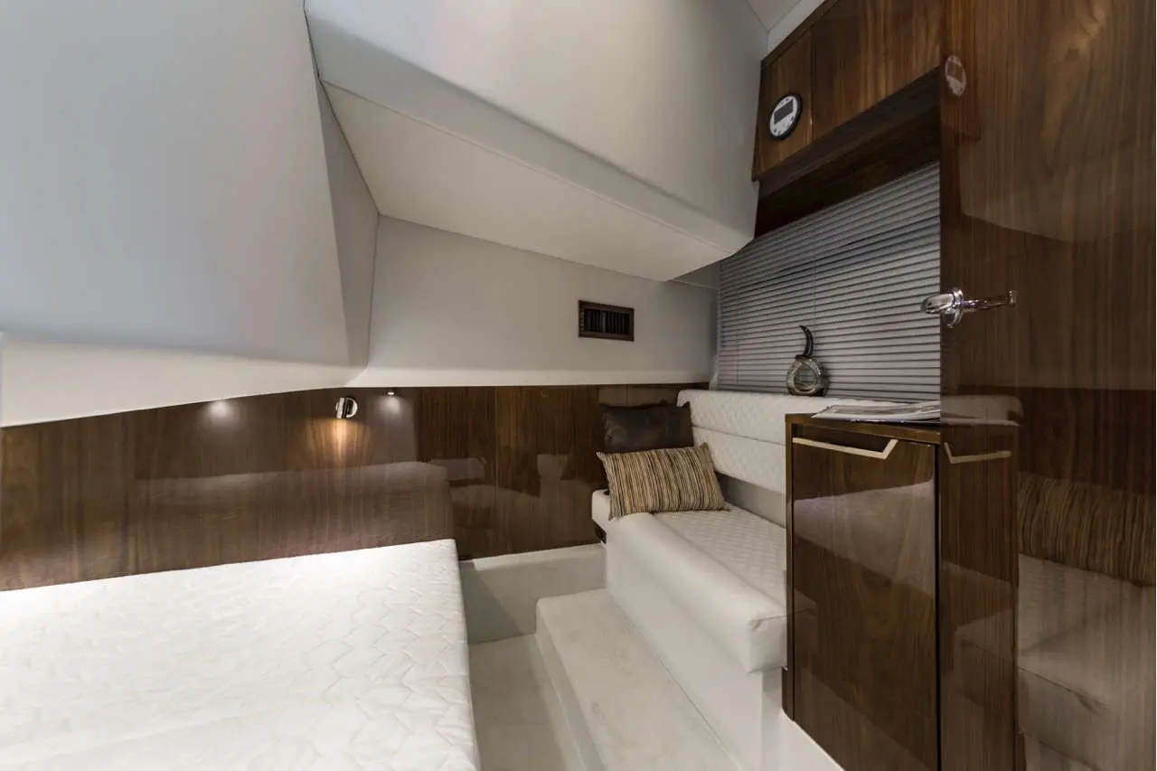 A modern, cozy yacht cabin featuring a white mattress, a brown wooden wall, decorative pillows, and stylish furnishings.
