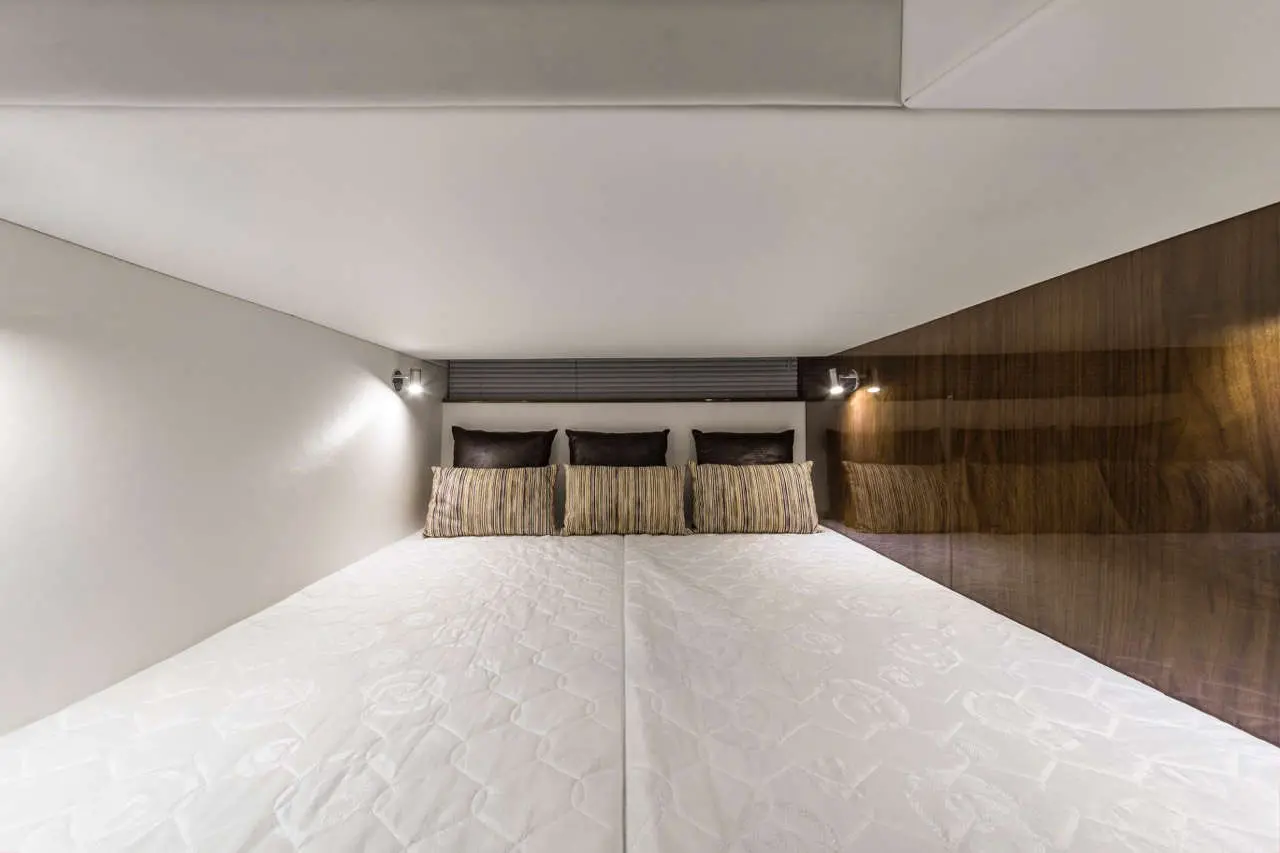 Modern bedroom with a large bed, featuring white bedding and decorative pillows, illuminated by wall-mounted lights.