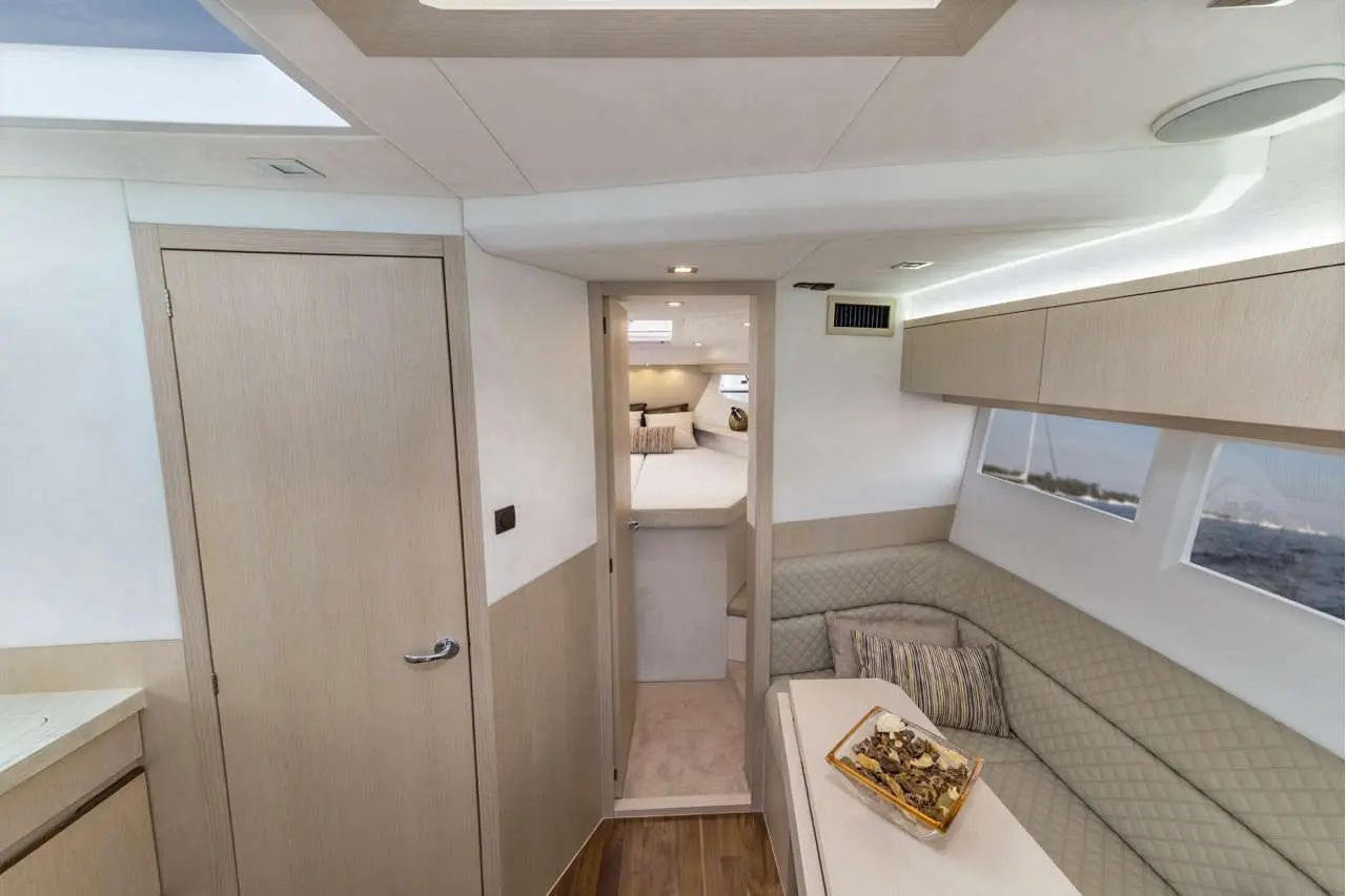 Interior of a modern boat featuring light wood finishes, a seating area with cushions, and a nearby doorway leading to a cabin.
