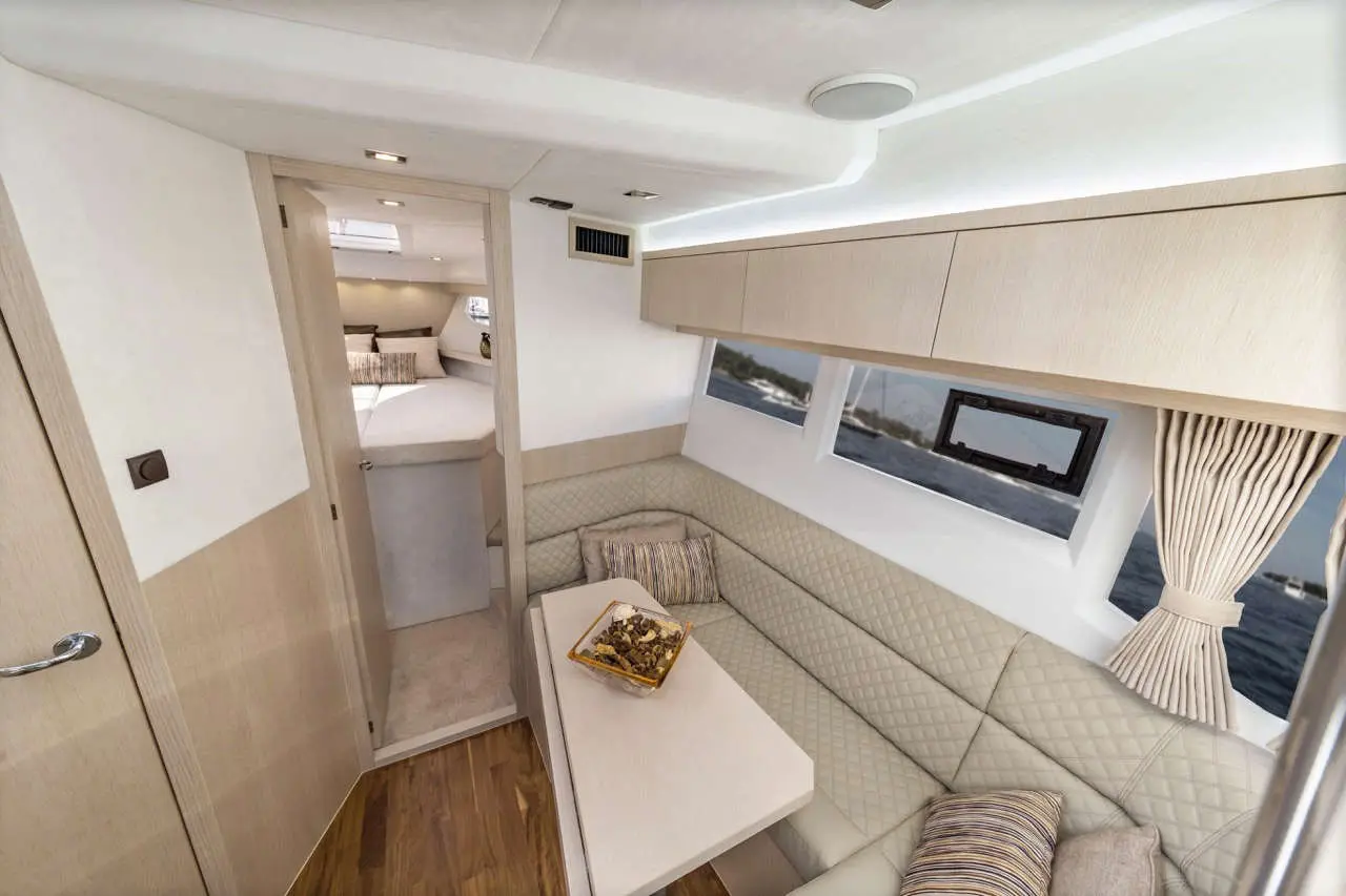 Modern yacht interior featuring a lounge area, light wood cabinetry, and a table with a bowl of snacks, overlooking water views.