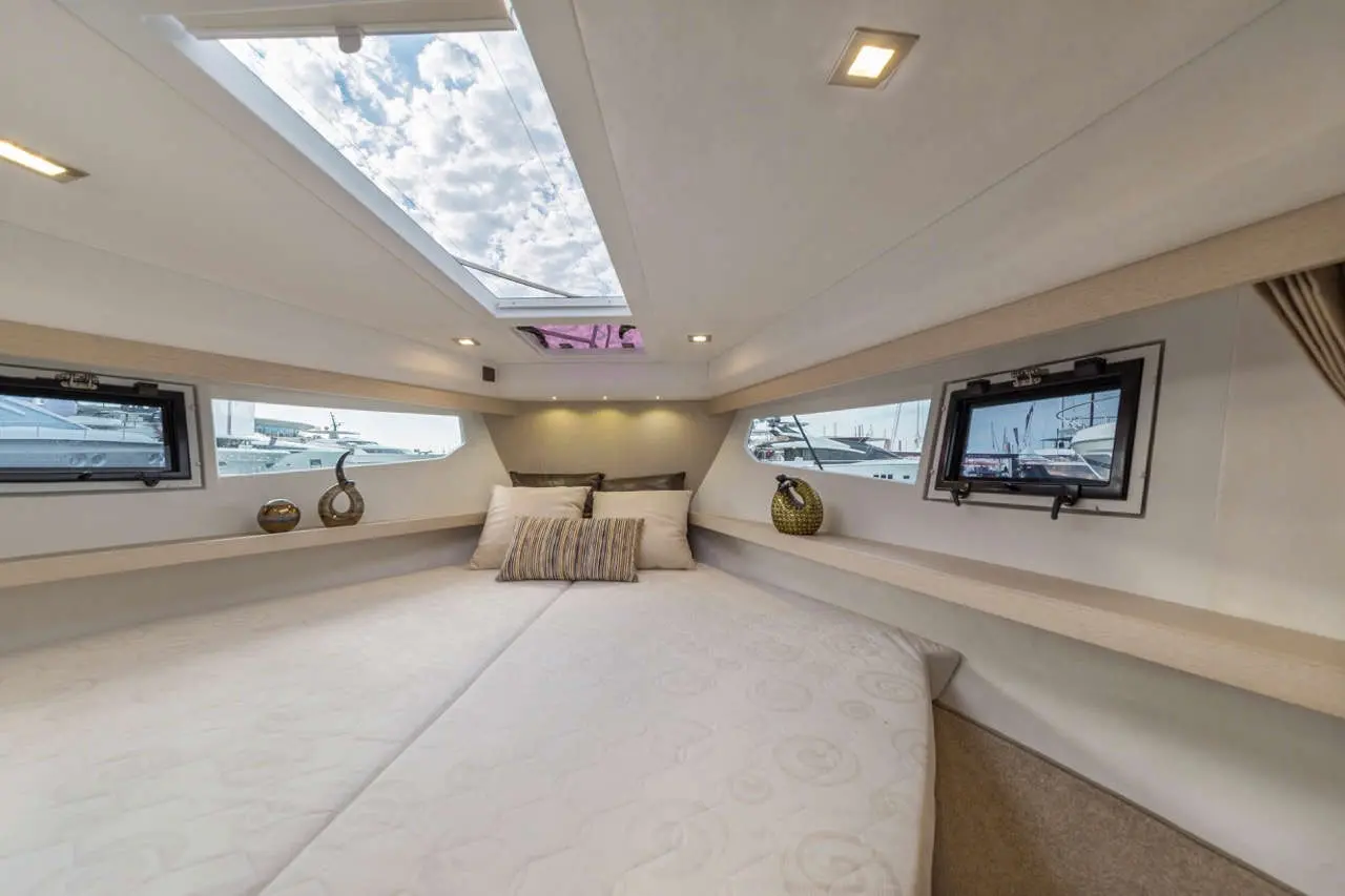 Spacious yacht cabin featuring a large bed, decorative pillows, and windows with views of the marina and cloudy sky.