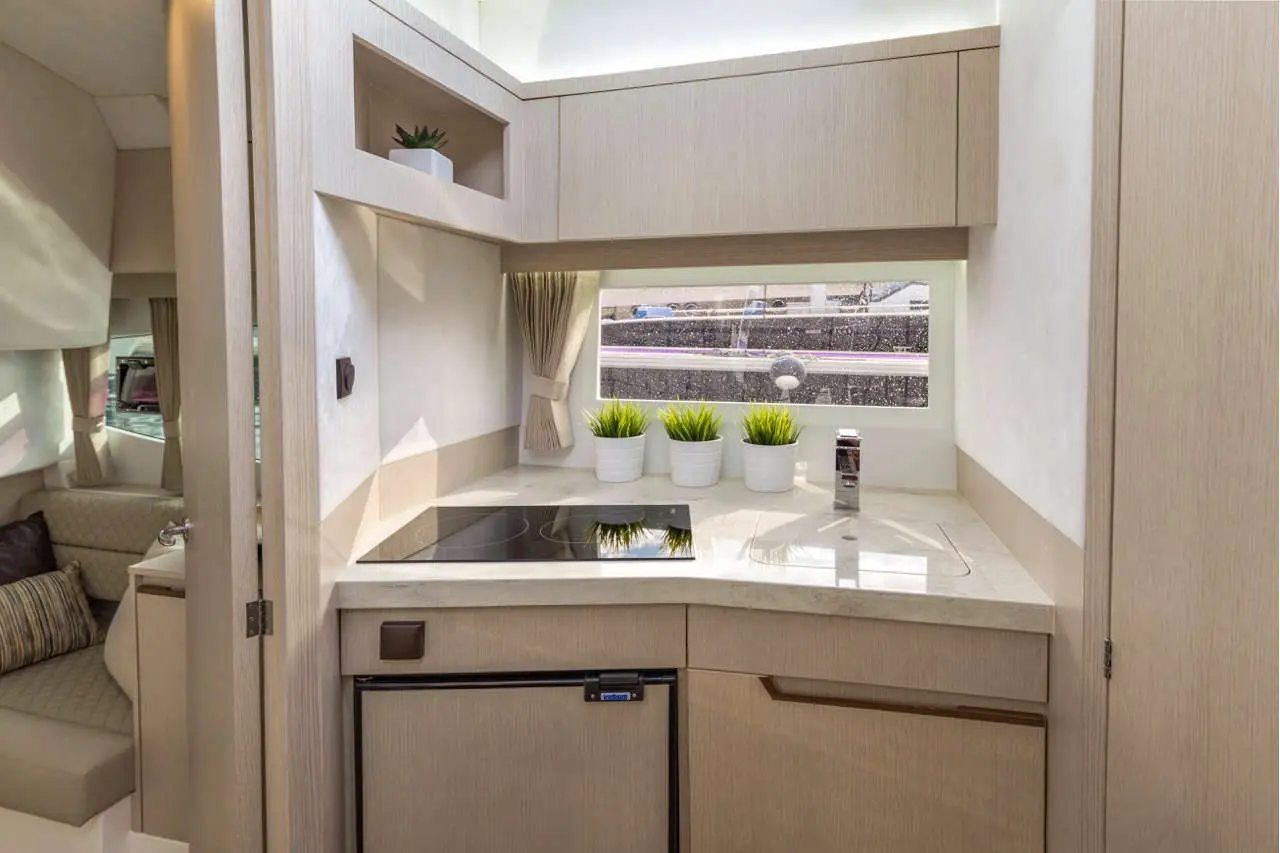Modern boat kitchen with stovetop, sink, white cabinetry, potted plants, and bright natural light from a window.