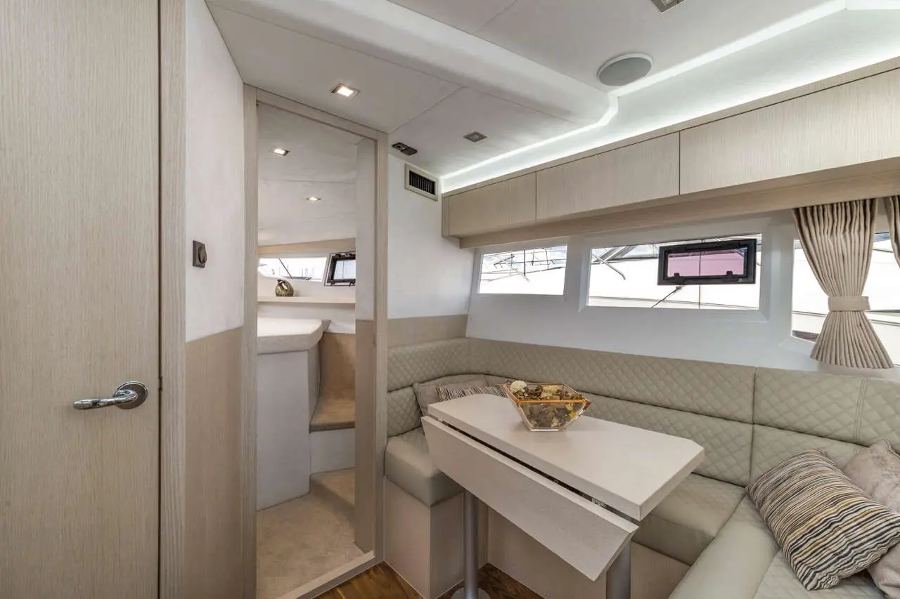 Interior of a sleek yacht featuring a light-coloured seating area, a white table, and a view through large windows.