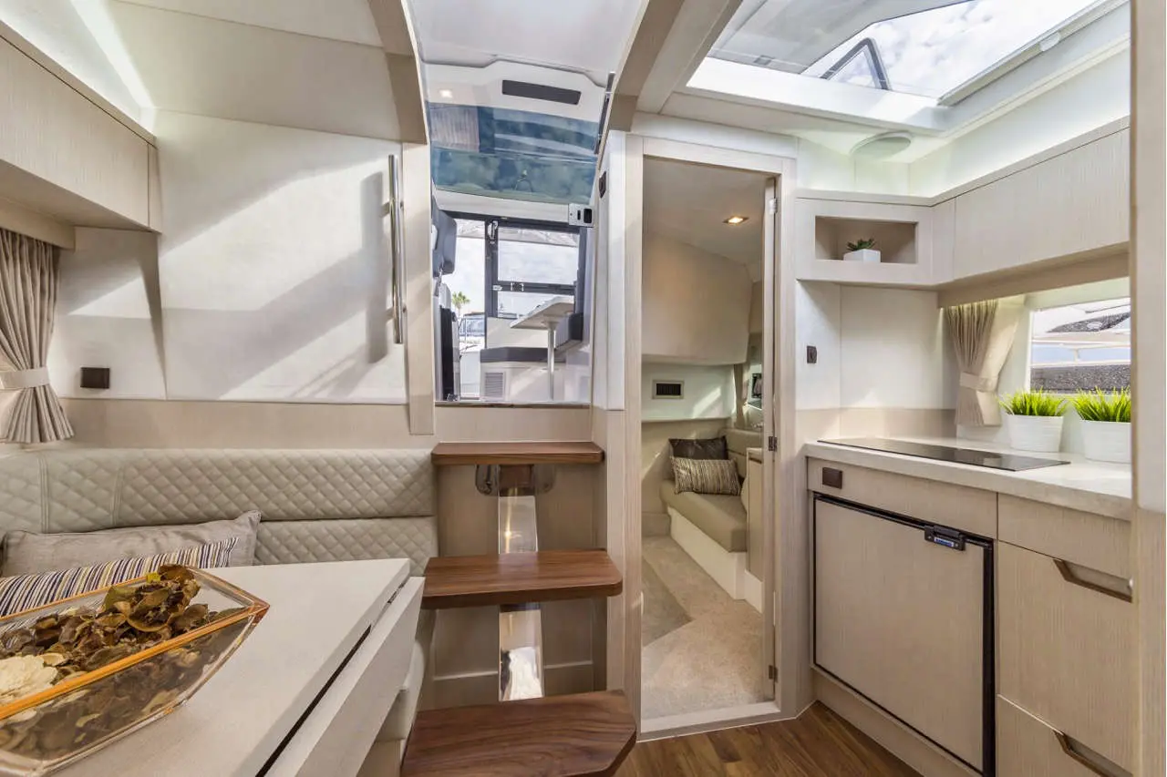 Modern yacht interior featuring a kitchenette, seating area, and stairway, with natural light from overhead windows.