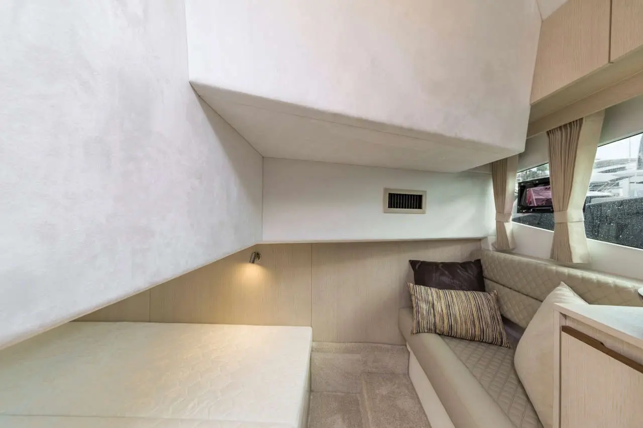 Modern boat interior featuring a compact seating area, textured walls, and a cushioned bed, with subtle lighting and windows.