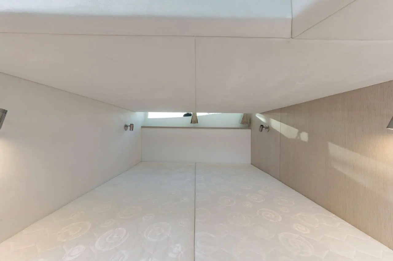 Interior view of a modern cabin with two white mattresses, soft lighting, and a small window above.