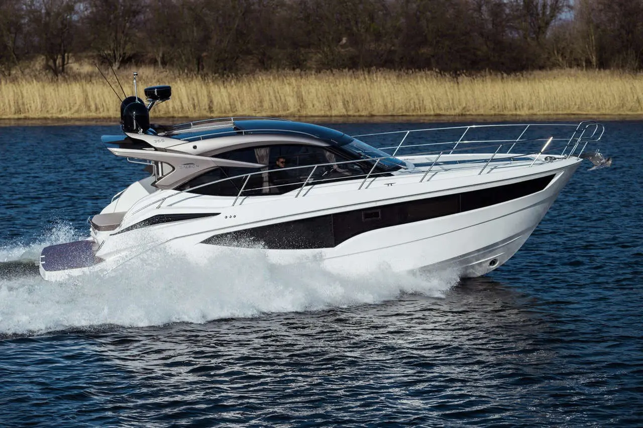 A sleek white yacht speeds across a blue lake, creating splashes of water, with a pilot visible in the cockpit.