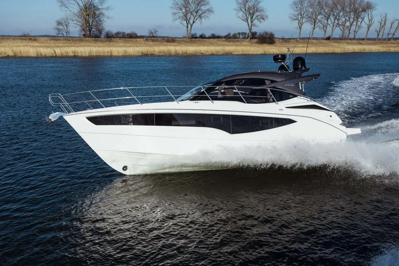 A sleek white yacht navigates through calm waters, surrounded by trees and grass, showcasing luxury boating.