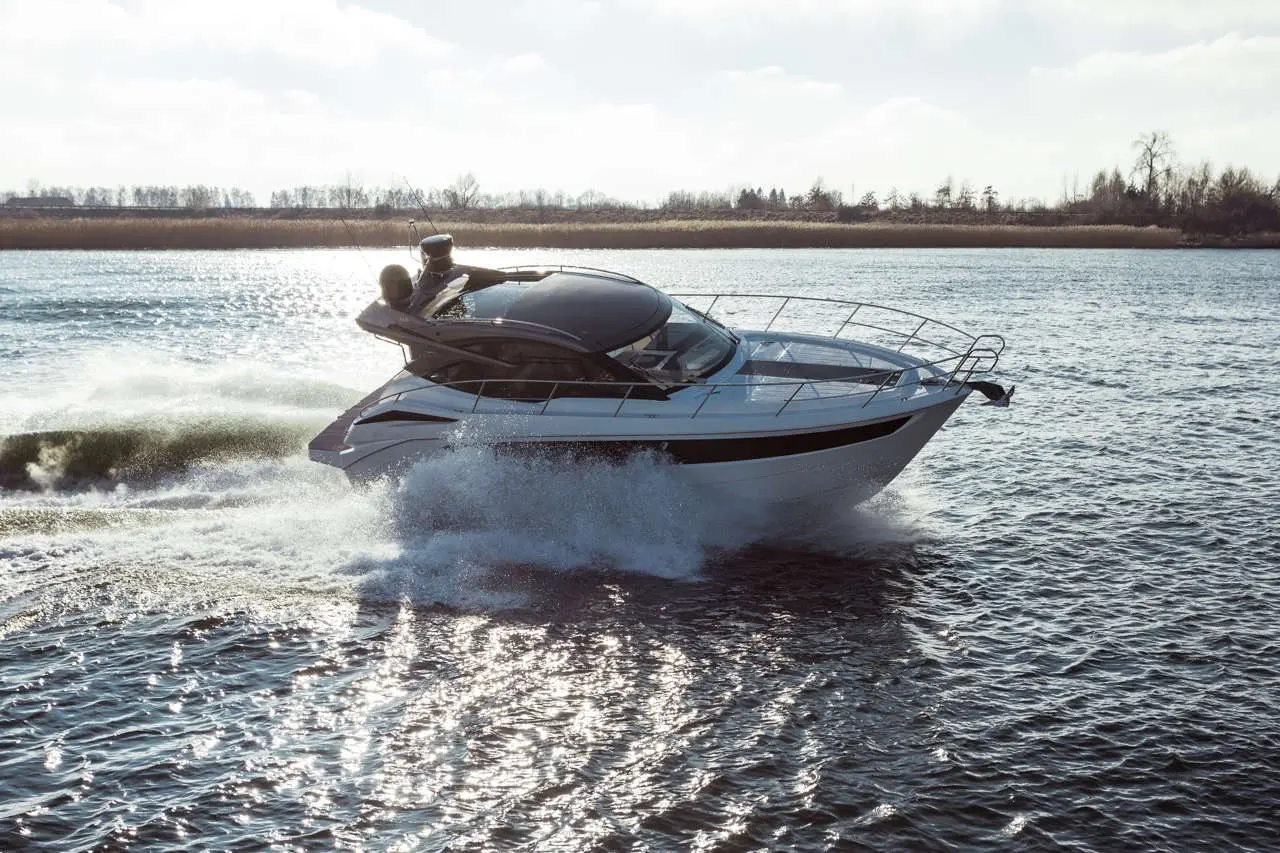 A luxury motorboat glides swiftly across a shimmering water surface, creating splashes and waves in a scenic riverscape.