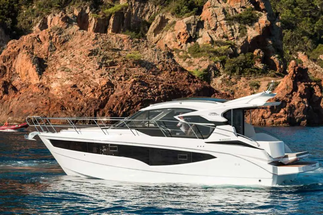 Luxury motor yacht cruising in clear blue water near rocky cliffs, showcasing a sleek design and modern features.