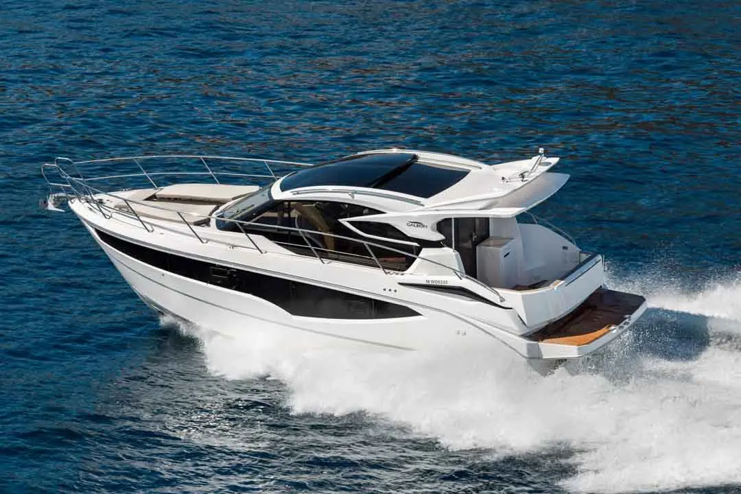 A sleek white motorboat navigates through clear blue waters, creating waves behind as it speeds along.