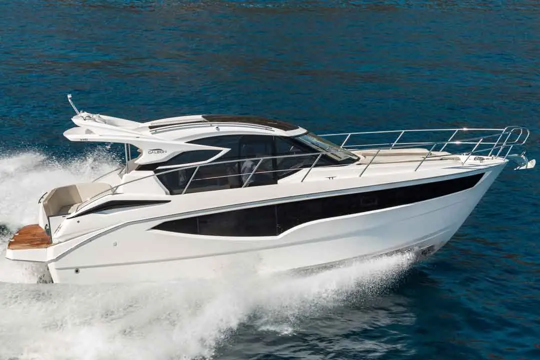 A sleek white motorboat cruising over blue water, creating waves with a modern design and large windows.