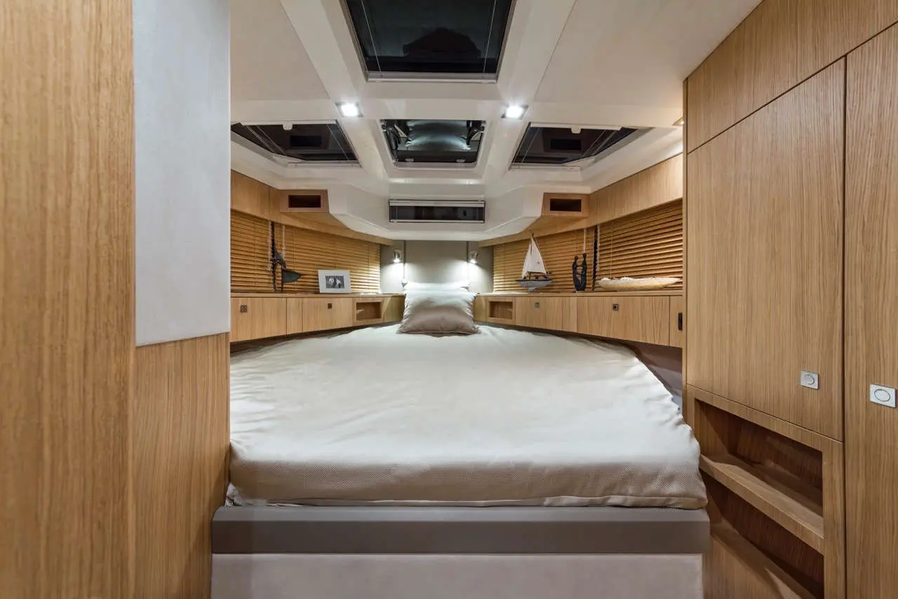 Modern yacht bedroom featuring a central double bed, wooden cabinetry, and skylights for natural light.