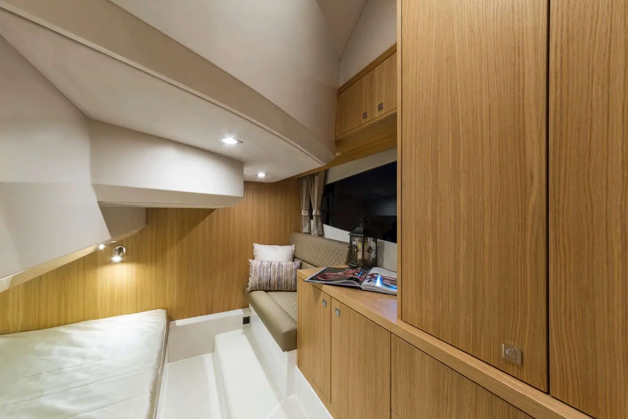 Interior of a cozy yacht cabin featuring wood paneling, a sofa, and a reading area with a magazine on a table.