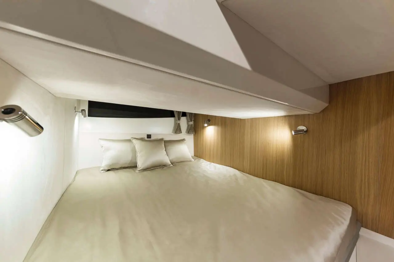 Compact modern cabin bedroom with a queen-sized bed, plush pillows, wooden walls, and adjustable wall lights.