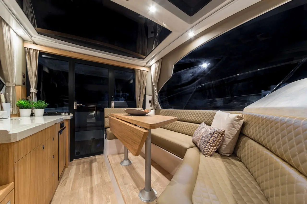 Luxurious yacht interior featuring a sleek dining area, large windows, and a wooden table with decorative bowl and cushions.