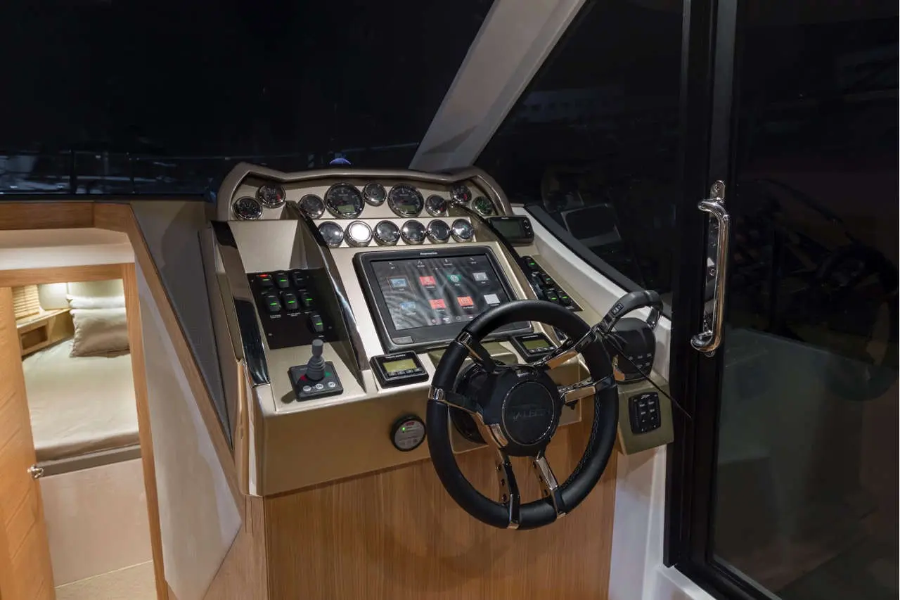 Boat cockpit featuring a steering wheel, control panel with gauges, touchscreen display, and access to a cabin.