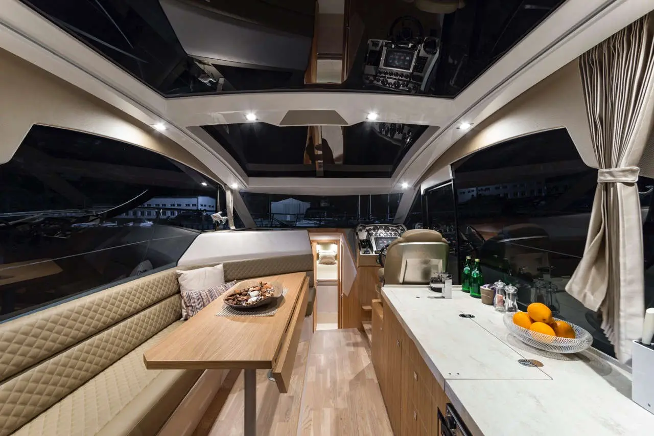 Luxurious yacht interior showcasing a dinette, steering area, modern decor, and a counter with drinks and fruit.