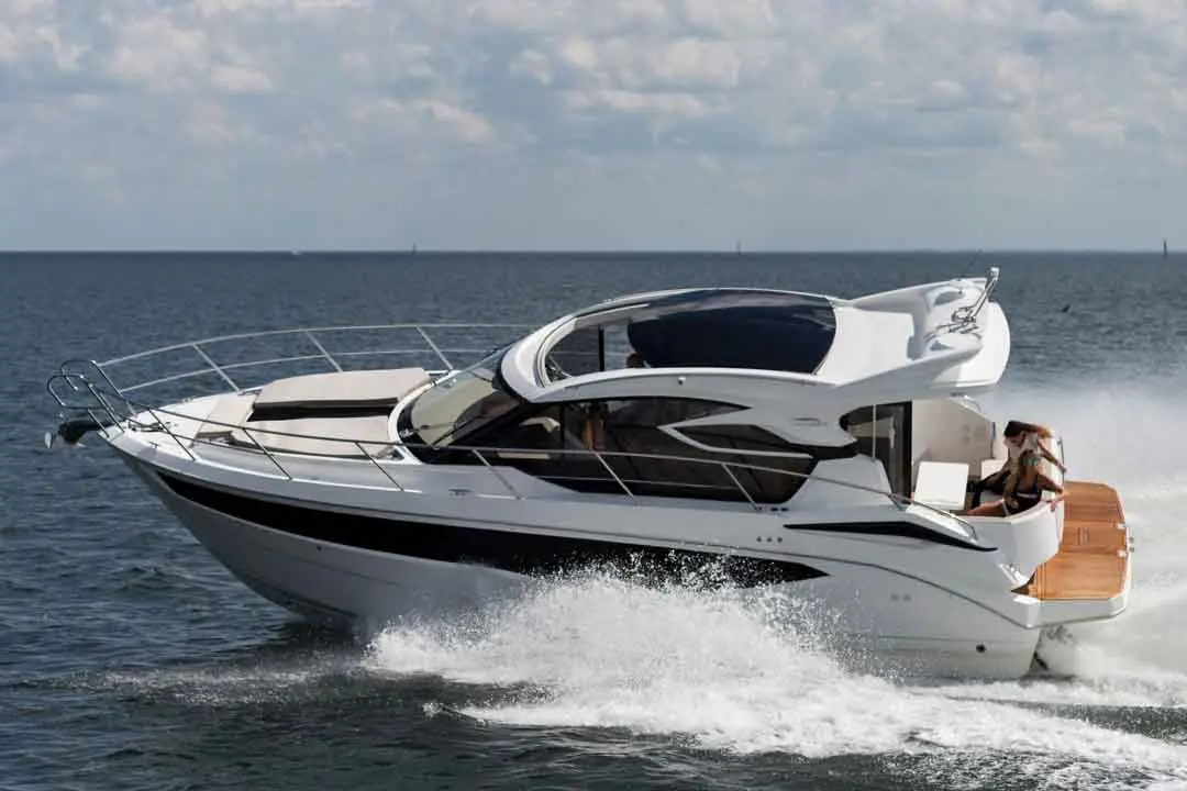 A sleek white motor yacht navigates through the sea, leaving a trail of water spray, with a woman seated at the rear.