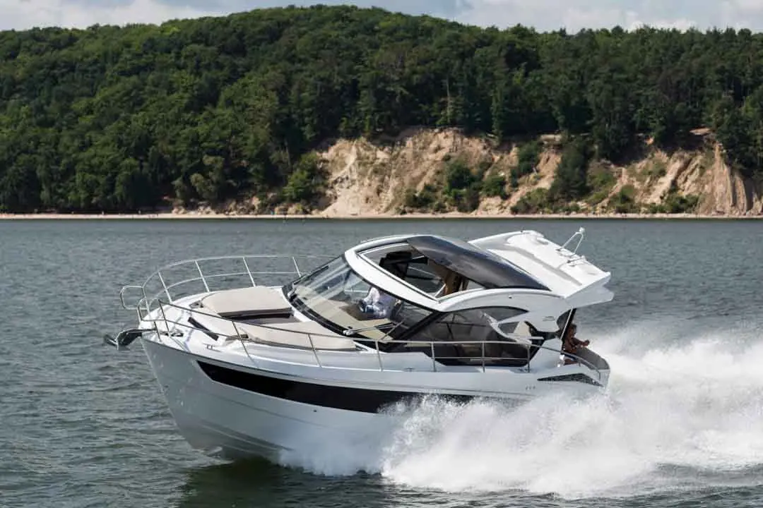 A sleek white boat cruising on a lake, creating splashes with its wake, set against a lush green hillside.