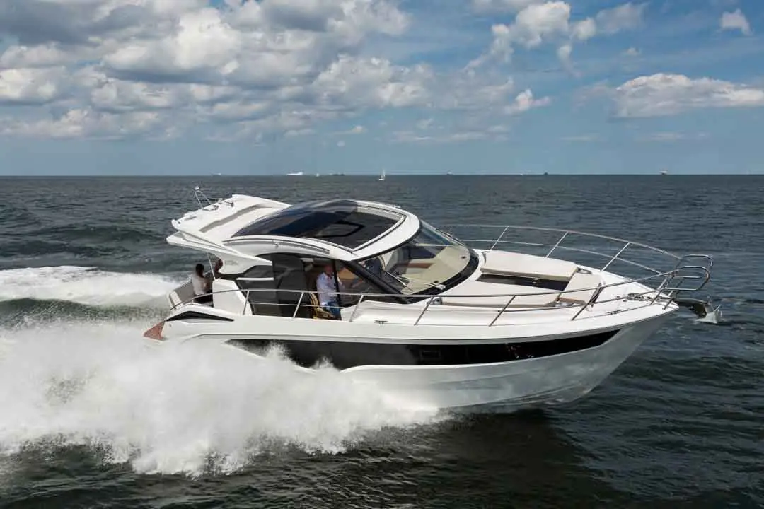 A white motorboat speeds across the waves under a partly cloudy sky, with two people visible on board.
