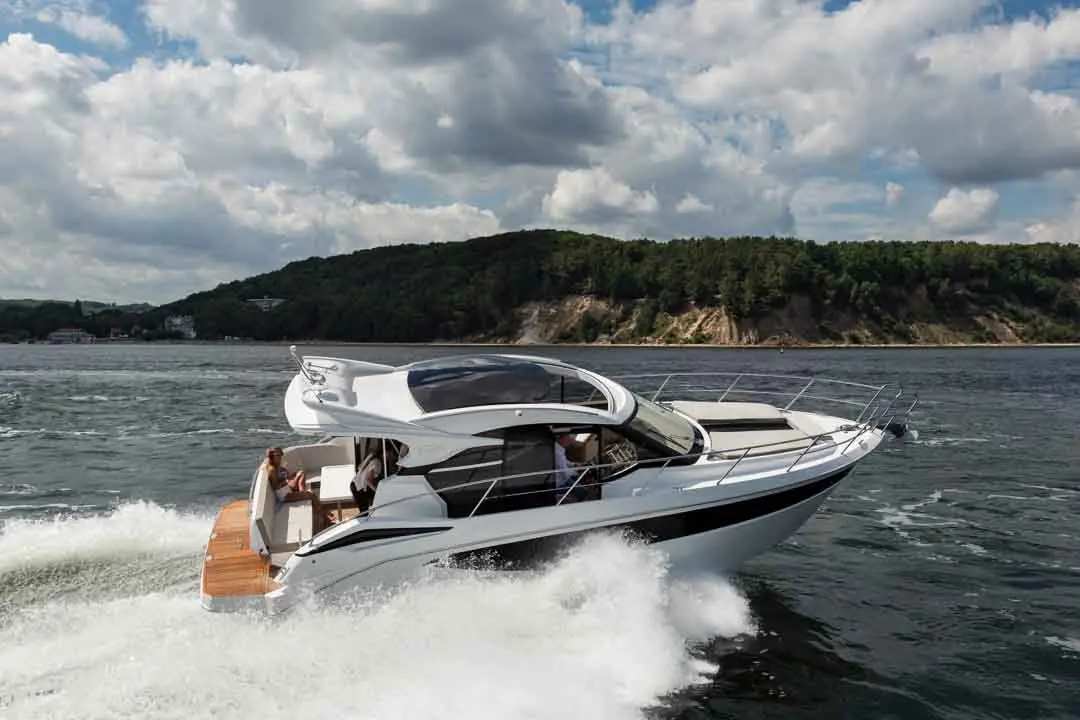 A luxury motorboat cruising on water with scenic green hills and clouds in the background, showcasing outdoor leisure activities.