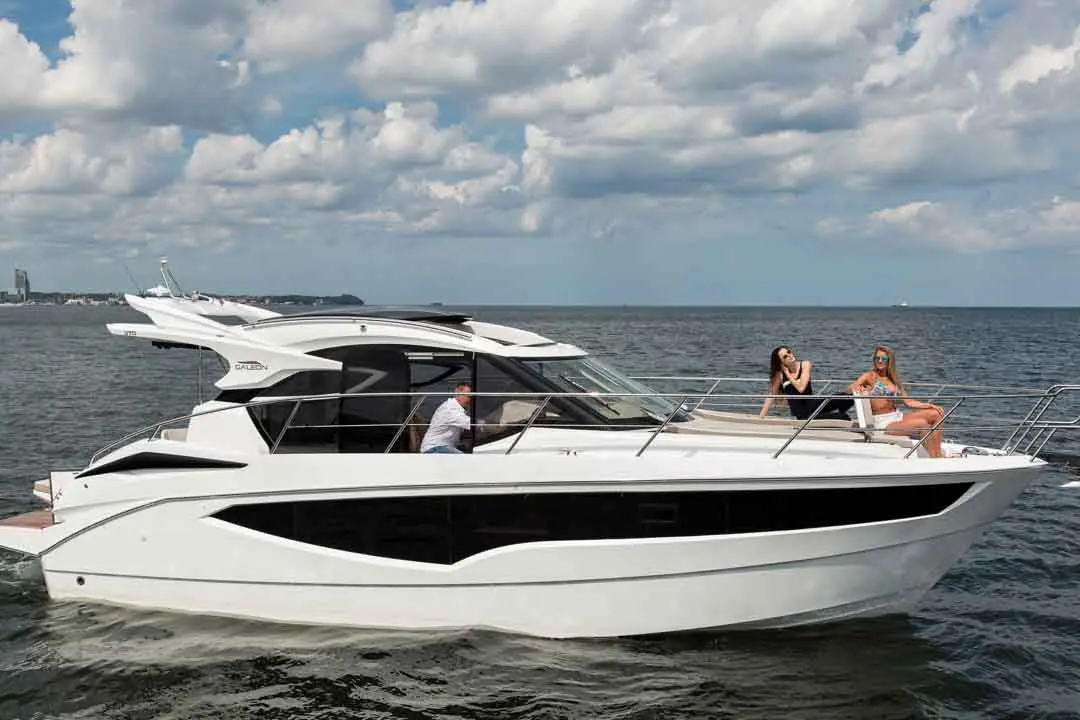 A stylish white motorboat glides on calm waters with three people on board, enjoying a sunny day on the water.
