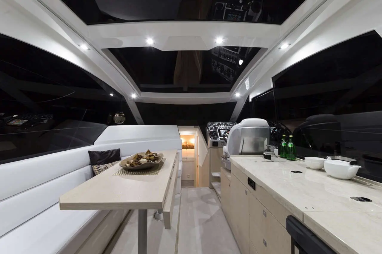Interior of a luxury boat featuring a dining area, galley, and controls, with a table set and drinks on the counter.