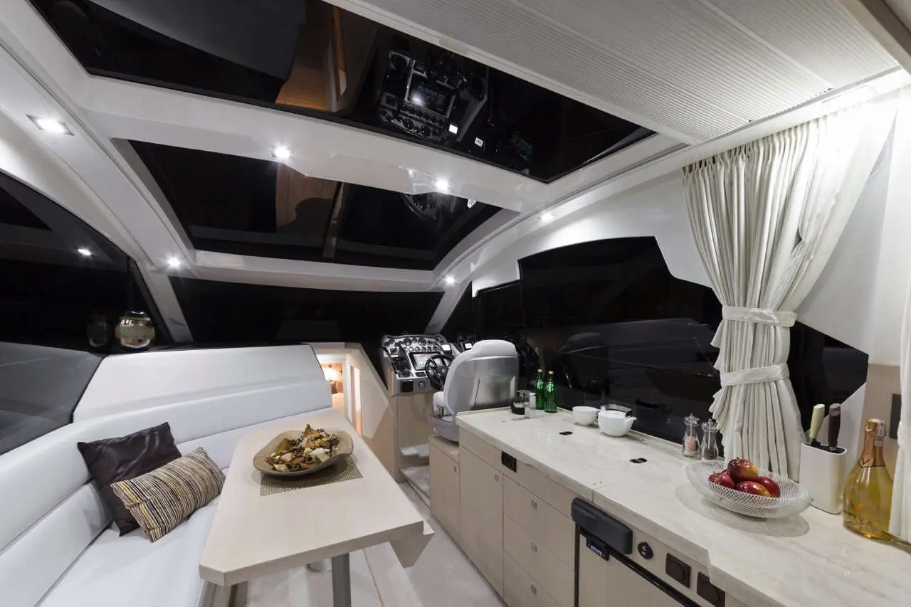 Modern boat interior featuring a dining area, sleek kitchen with drinks, and large windows for ample natural light.