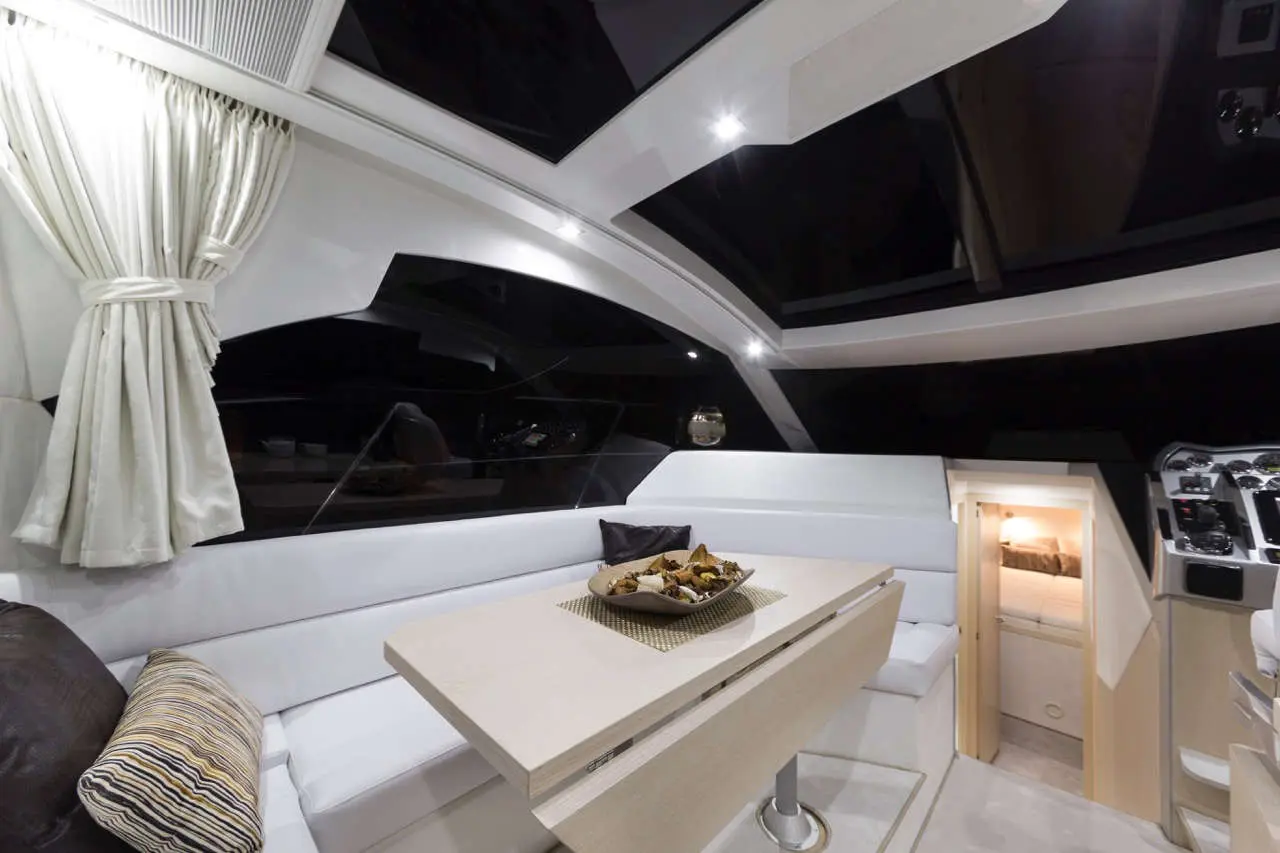 Luxurious yacht interior featuring a sleek dining table with dry fruit, plush seating, and large windows creating an airy atmosphere.