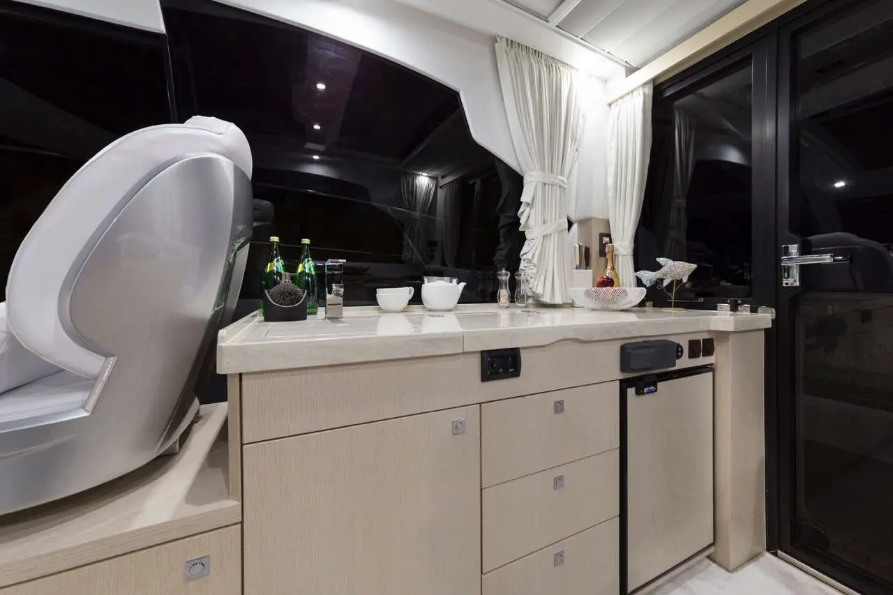 Luxury yacht interior featuring a modern bar area with bottles, glasses, and a fridge, illuminated by soft lighting.