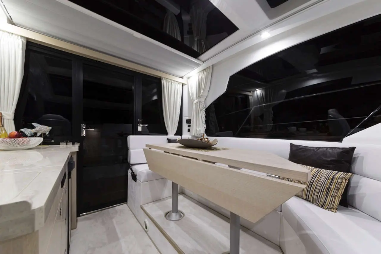 Stylish yacht interior featuring a beige dining table, white seating, and large glass doors, illuminated by soft lighting.