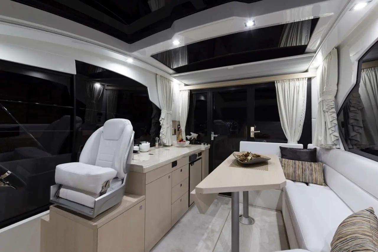 A sleek boat interior featuring a white captain's chair, table, and comfortable seating with natural light from large windows.