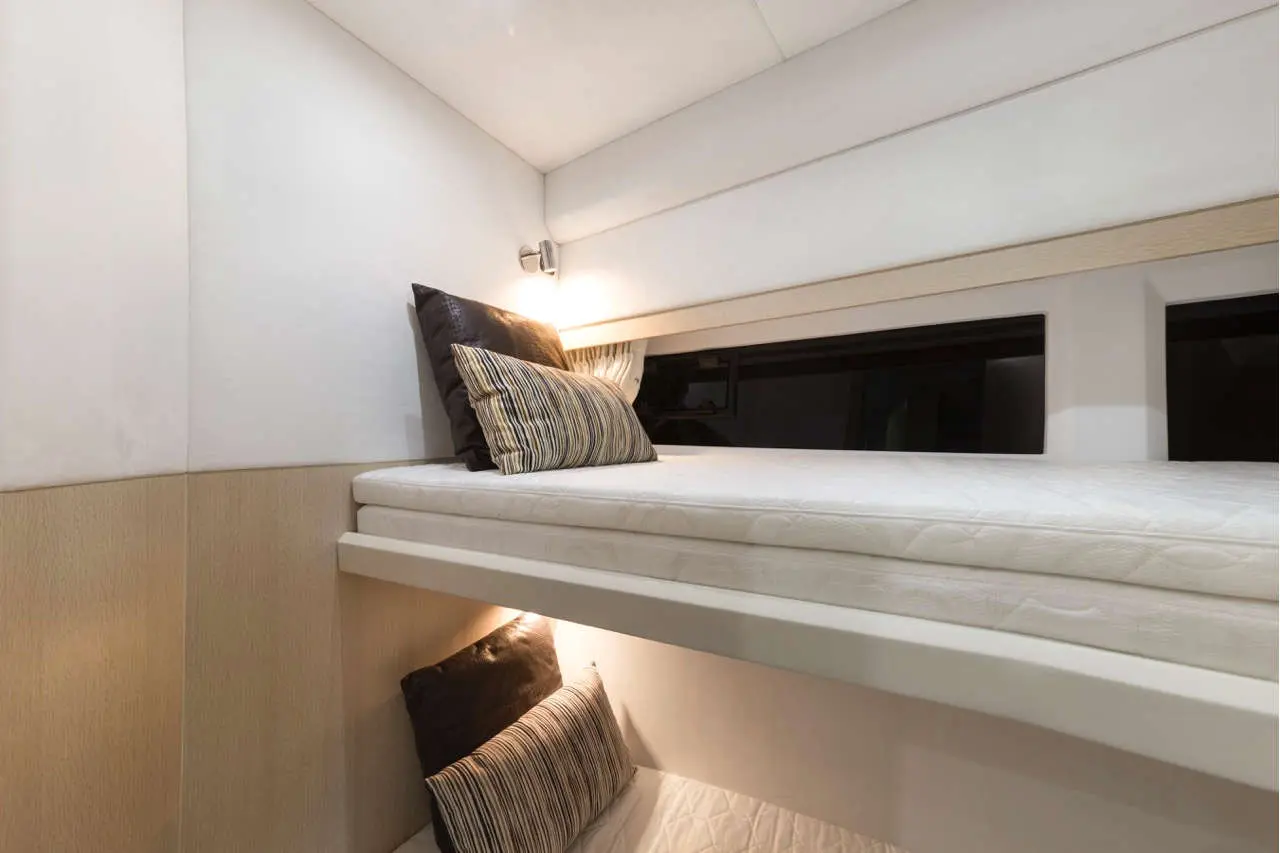 A modern bunk bed with two mattresses, decorated with patterned and solid colour cushions, in a minimalist room design.