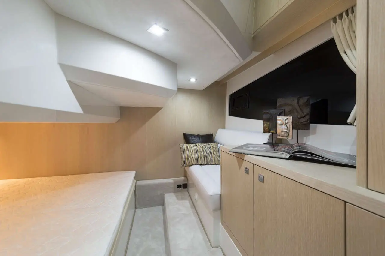 Modern yacht interior with a cozy seating area, double bed, and decorative items on a wooden cabinet. Light colors and design.