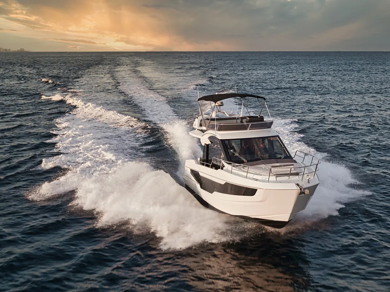 A sleek motorboat navigates through wavy waters under a dramatic sunset, leaving a frothy wake behind.