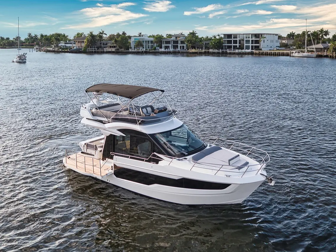 Luxury motorboat cruising on calm waters, surrounded by modern waterfront homes and palm trees under a blue sky.